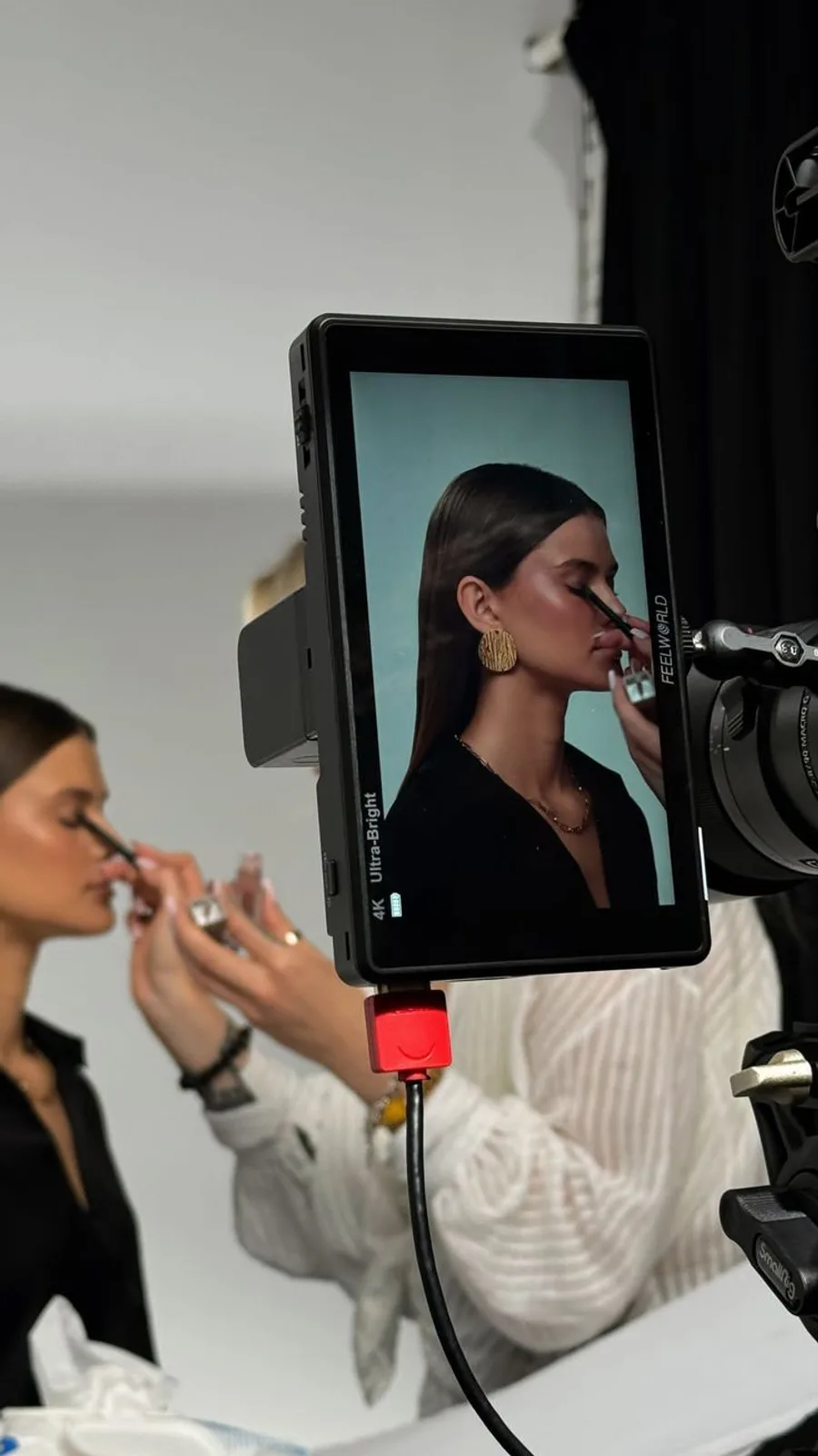 A camera monitor showing a model having makeup applied on a studio set