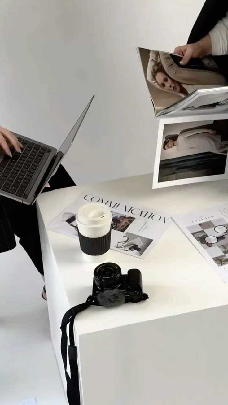 Creative workspace with laptop, camera, coffee, and brand communication mood boards on a white desk