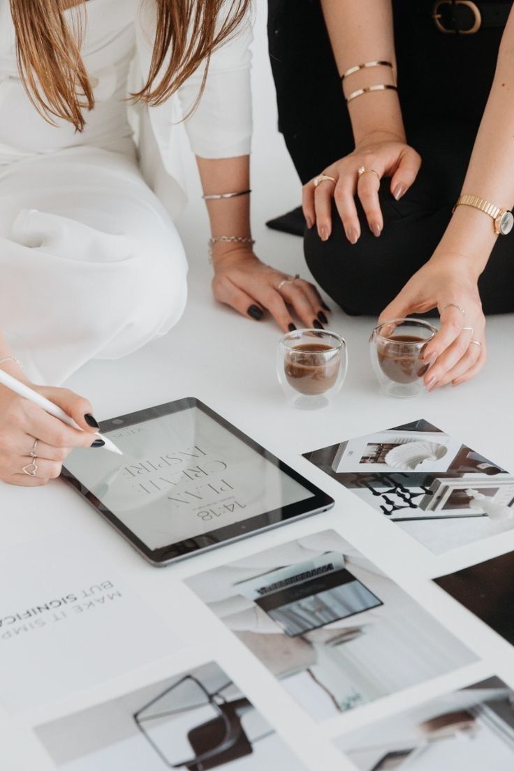 Two women reviewing creative work on a tablet over coffee
